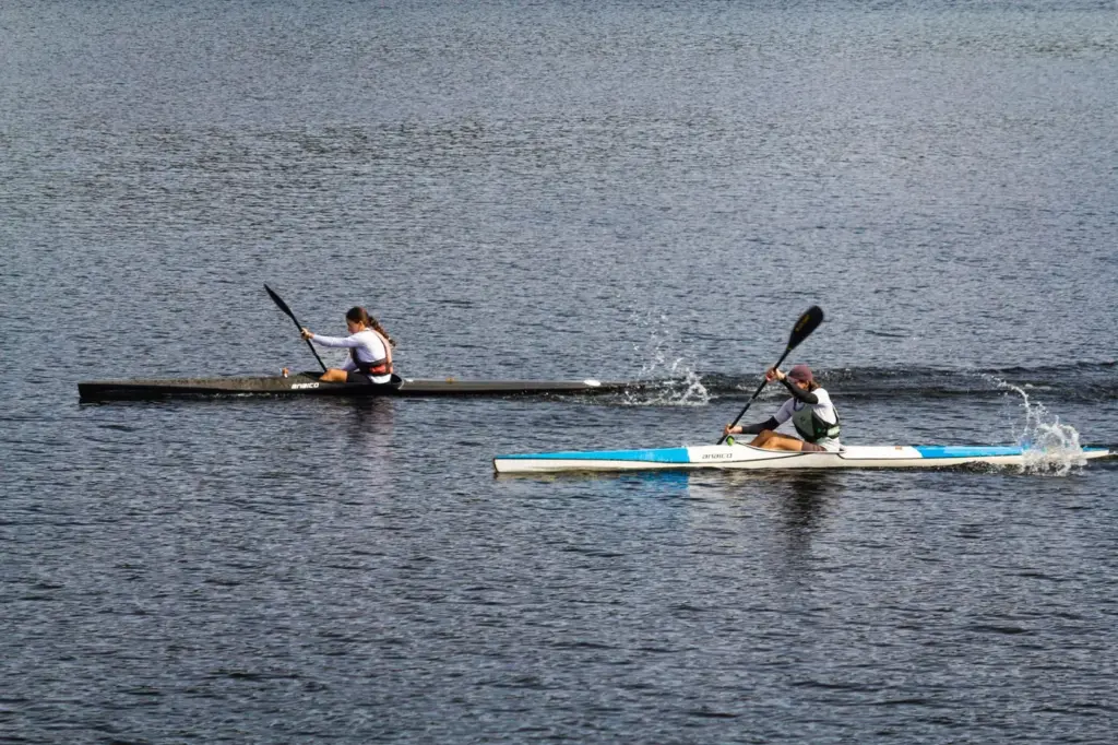 Zwei Athleten paddeln energisch in einem Kajakrennen auf einem ruhigen See und zeigen Wettbewerbsgeist und Agilität.