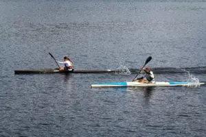 Zwei Athleten paddeln energisch in einem Kajakrennen auf einem ruhigen See und zeigen Wettbewerbsgeist und Agilität.