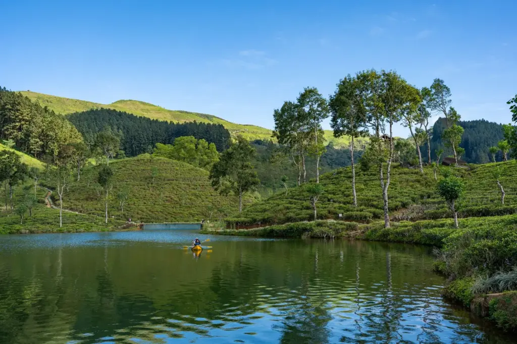 Idyllische Szene einer Person, die auf einem ruhigen See Kajak fährt, umgeben von üppigen grünen Hügeln und heiteren Lan